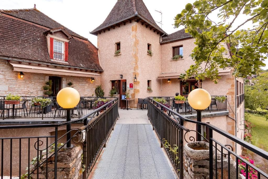 Stone building with outdoor dining terraces connected by a metal walkway in Loubressac.