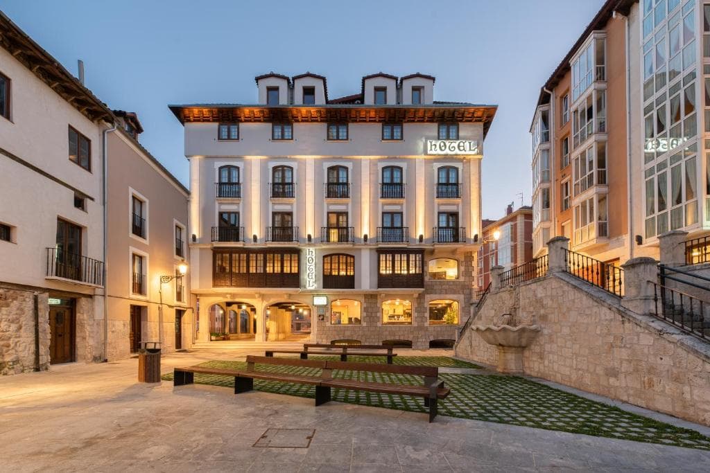 Hotel building illuminated at dusk in a town square with stone fountain and benches.