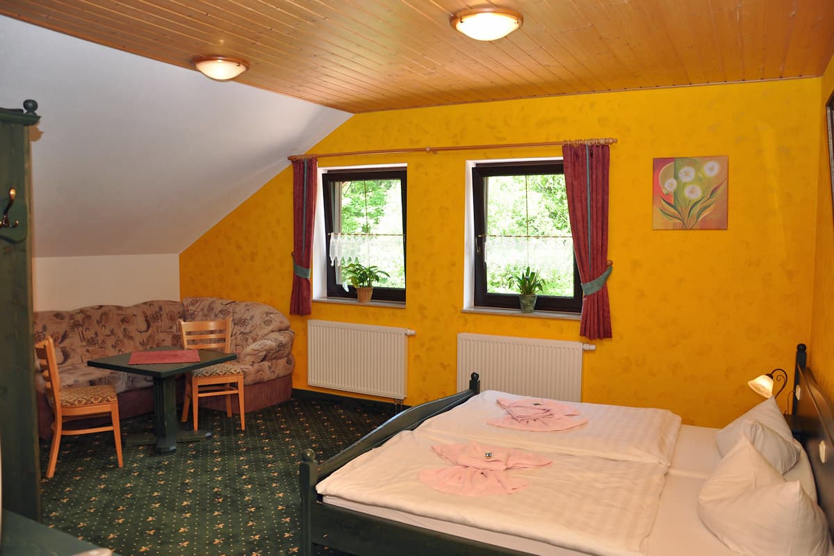 Guest room with yellow walls, wooden ceiling, double bed, and seating area at Hubertushaus.