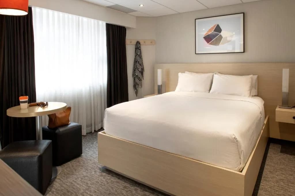 Modern hotel room with white bedding, light wood accents, and a window with dark curtains in Banff Aspen Lodge.