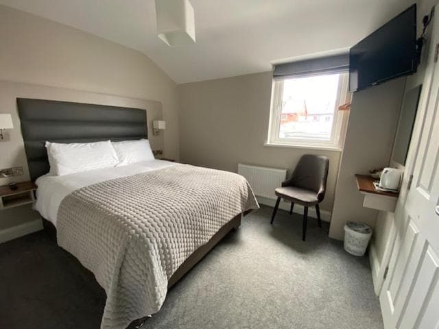 Double bed with white linens and textured grey throw in a modern guest room.