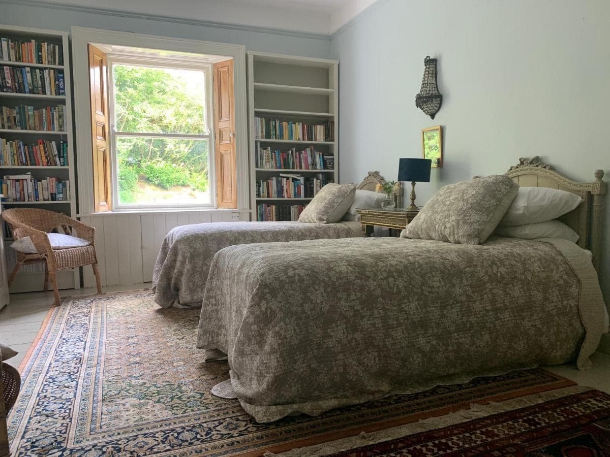 Twin beds in a bright room with built-in bookshelves and a window view of greenery.