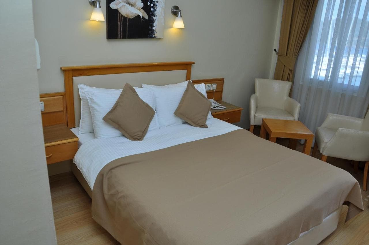 Hotel Doruk room with wooden headboard, white linens, beige accents, and sheer curtains.