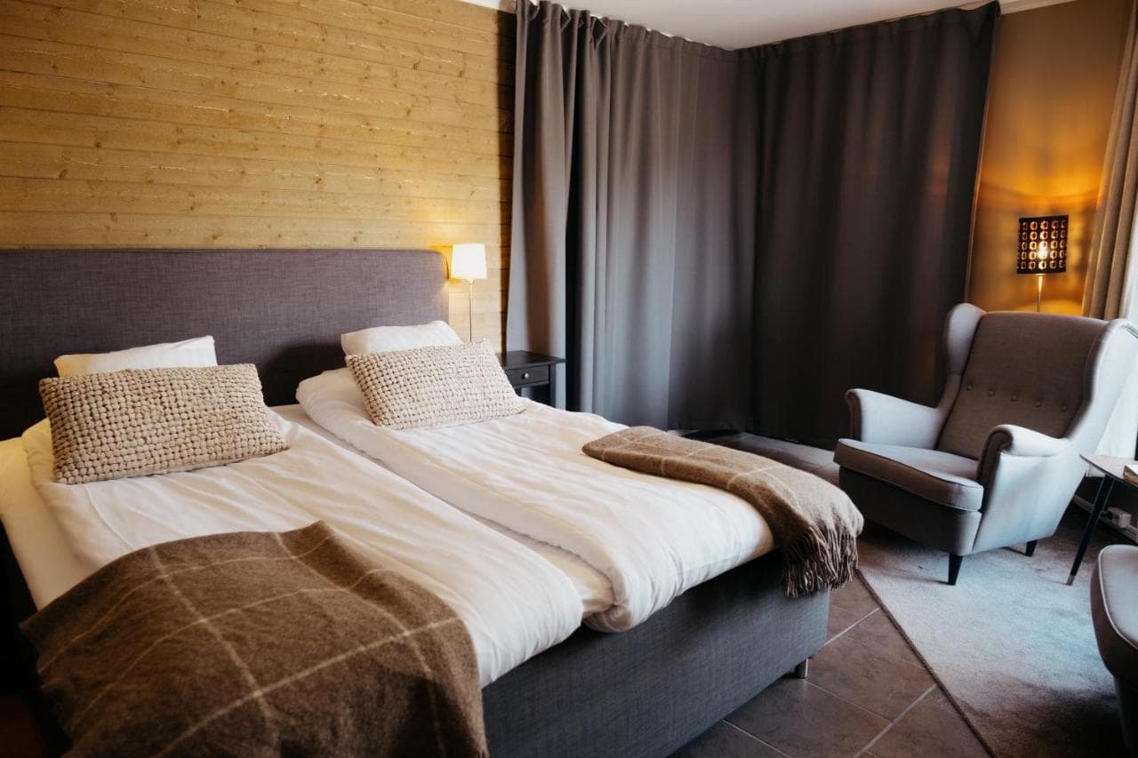 Twin beds with white linens and brown throws in Abisko Mountain Lodge room with wood wall.