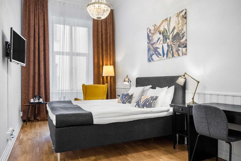 Hotel room with dark gray bed, yellow armchair, chandelier, and olive branch artwork.