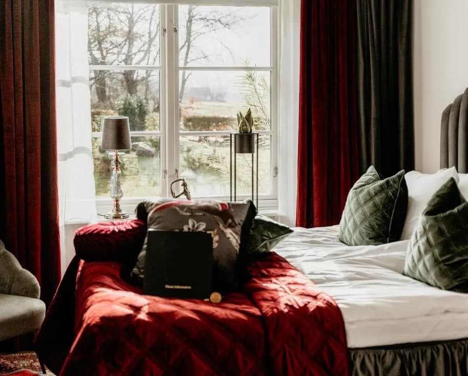 Bedroom with red bedding, green pillows, and large window overlooking trees at Villa Brunnby