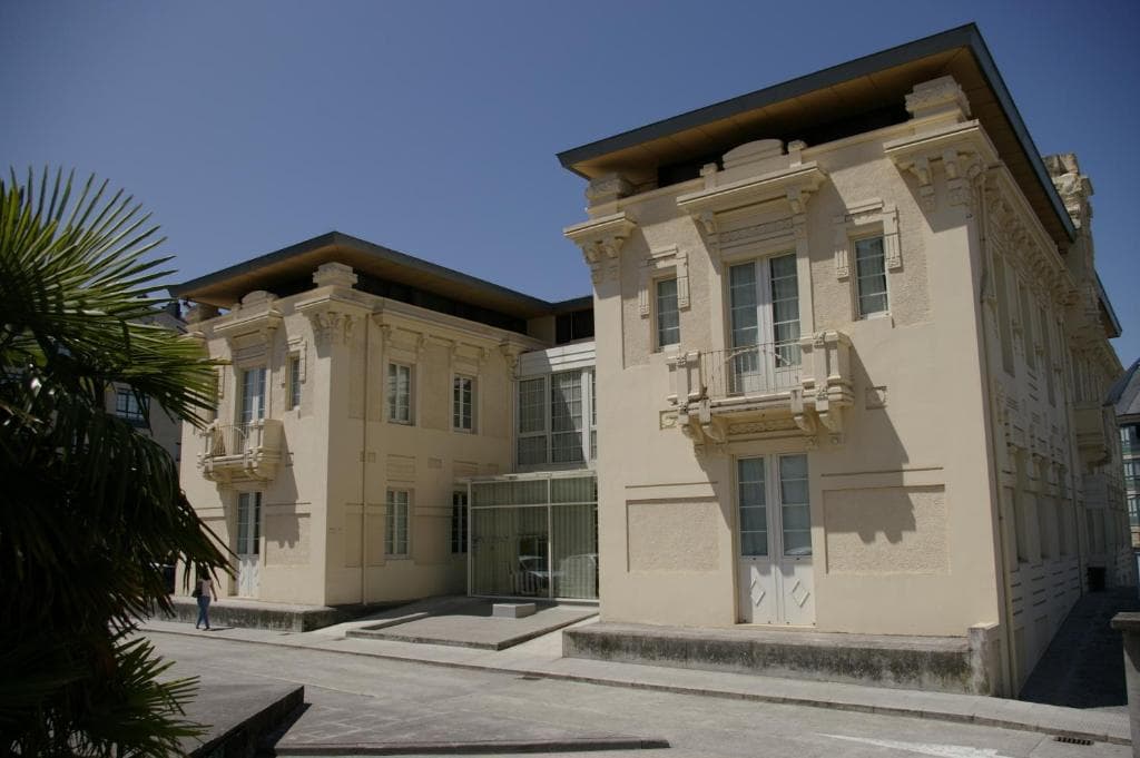 Hotel Villa De Betanzos building exterior with ornate facade and palm fronds on sunny day.