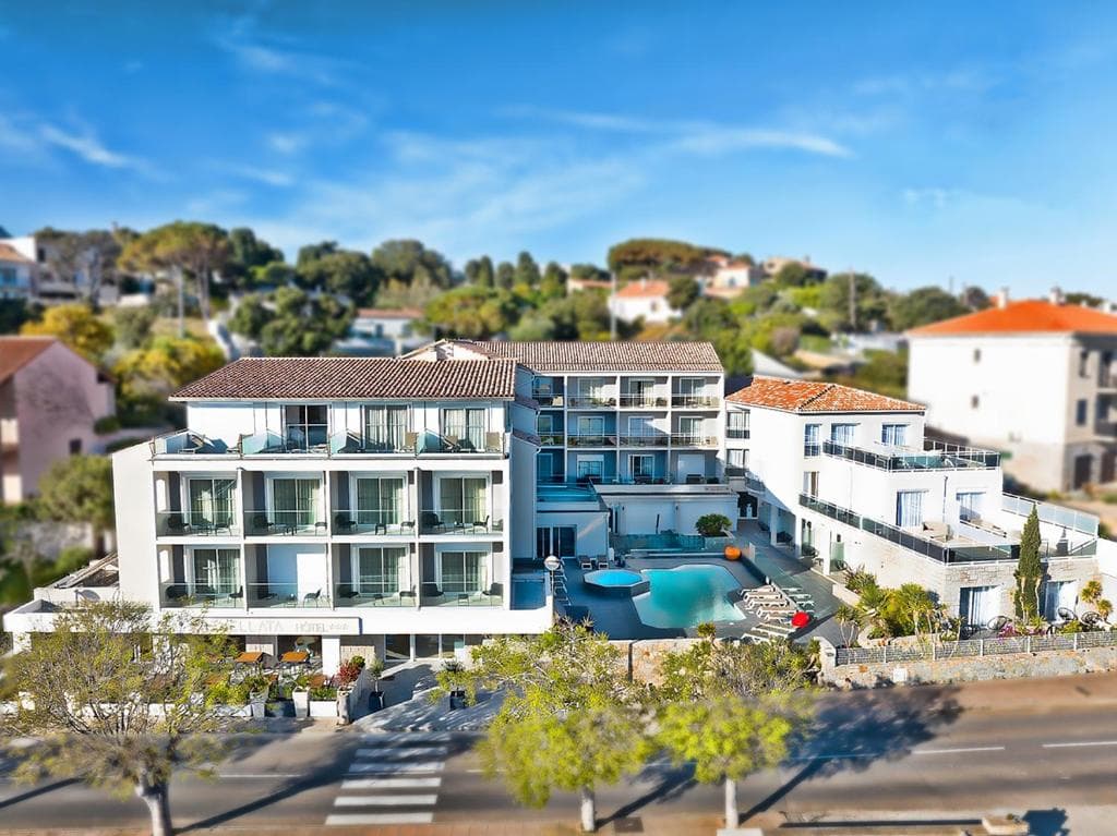 Hotel Revellata & Spa with white facade, balconies, and outdoor pool against a sunny, hilly backdrop.