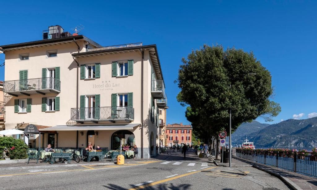 Hotel du Lac with outdoor dining, tree-lined street, and mountains across the lake in Menaggio.