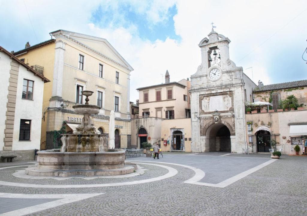 Stone fountain in town square with clock tower archway and surrounding historic buildings