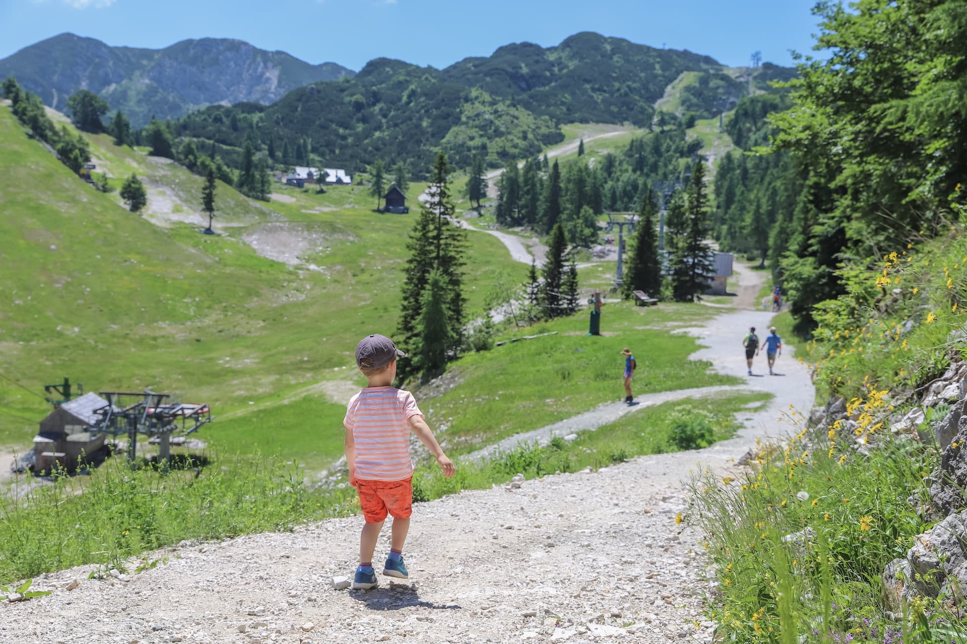 Child hiking on gravel path overlooking green mountain slopes with ski lift infrastructure.