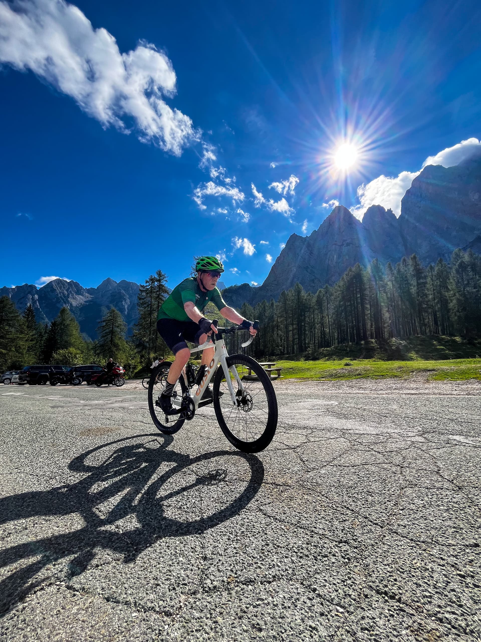 Cyclist riding a road bike on asphalt near mountains under a bright sunny sky with clouds.