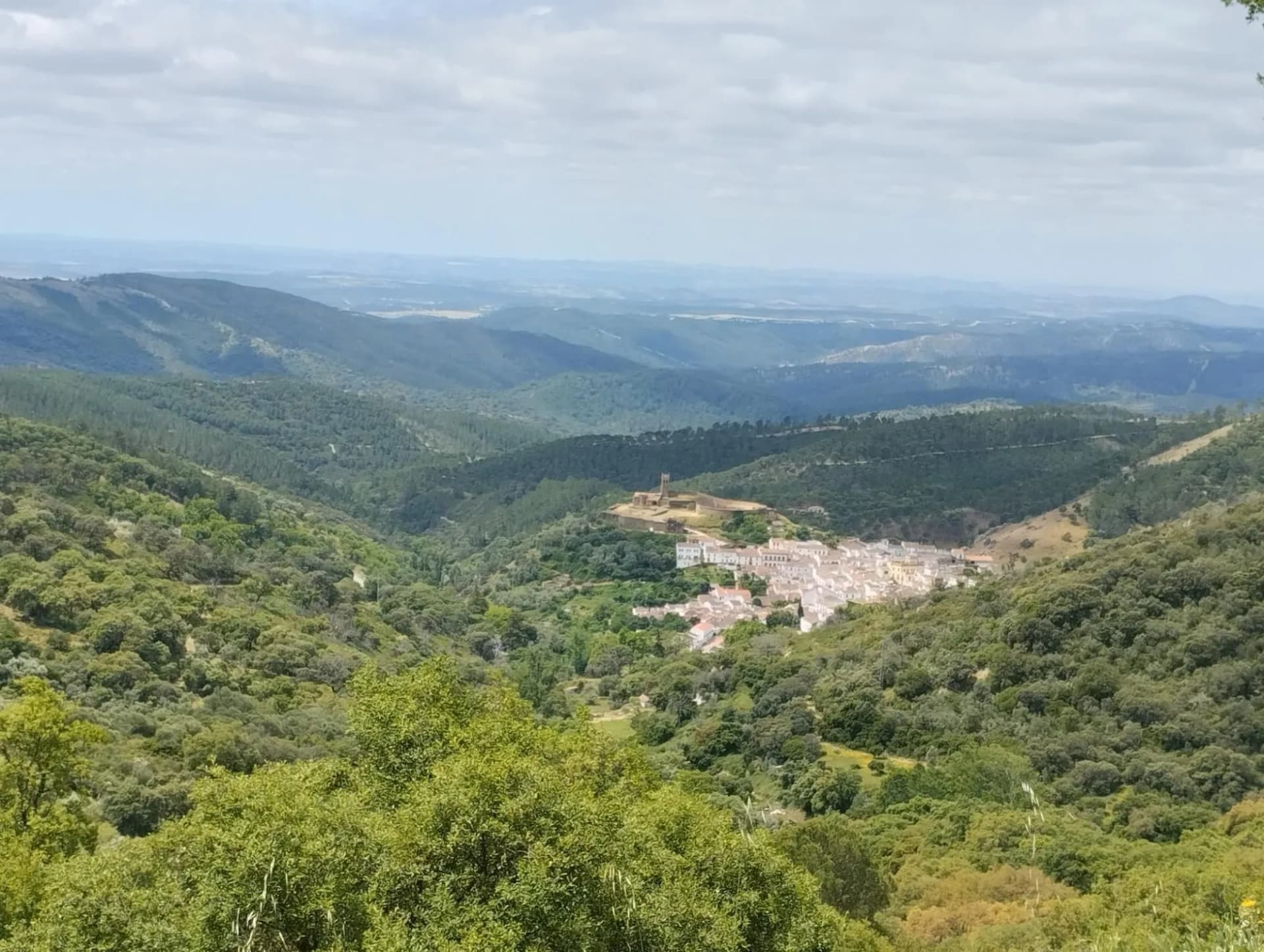 View from Cerro San Cristobal overlooking a white village nestled in lush green, rolling mountains.