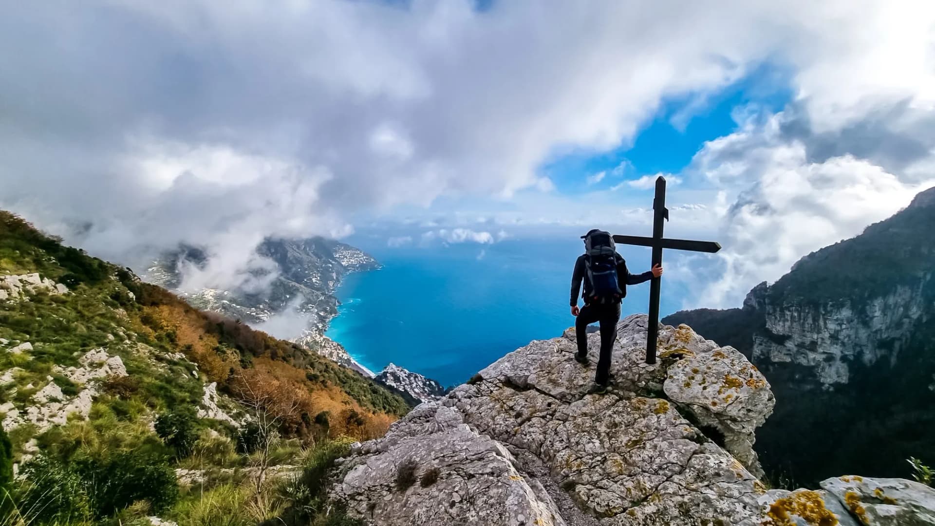 Active man at summit cross near Santa Maria del Castello. Scenic view on coastal town Positano, Praiano. Magical hiking trail, Lattari Mountains, Apennines, Amalfi Coast, Campania, Italy, Europe