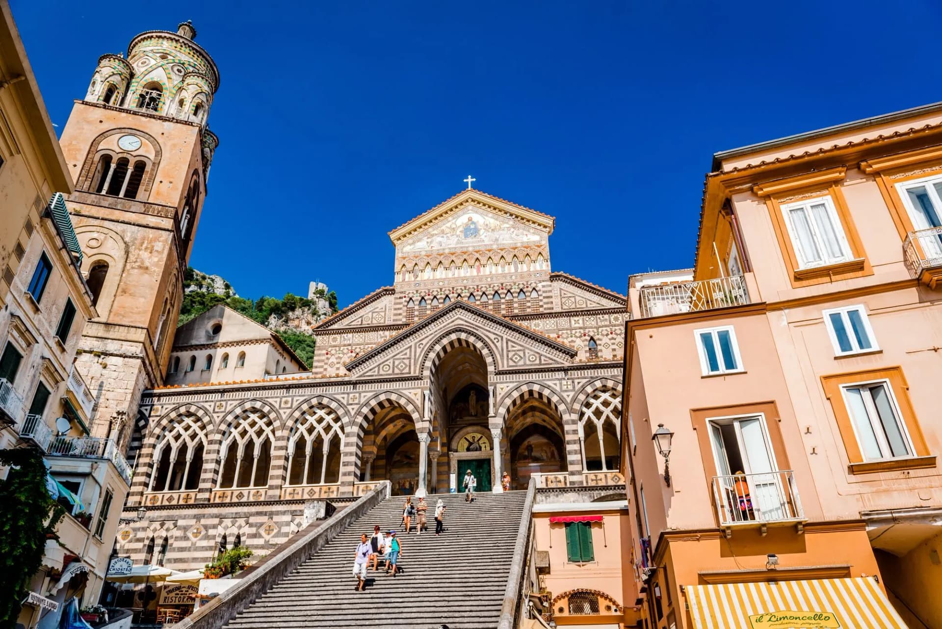 Cathedral of St. Andrea in Amalfi with striped facade and bell tower, viewed from below stone steps.