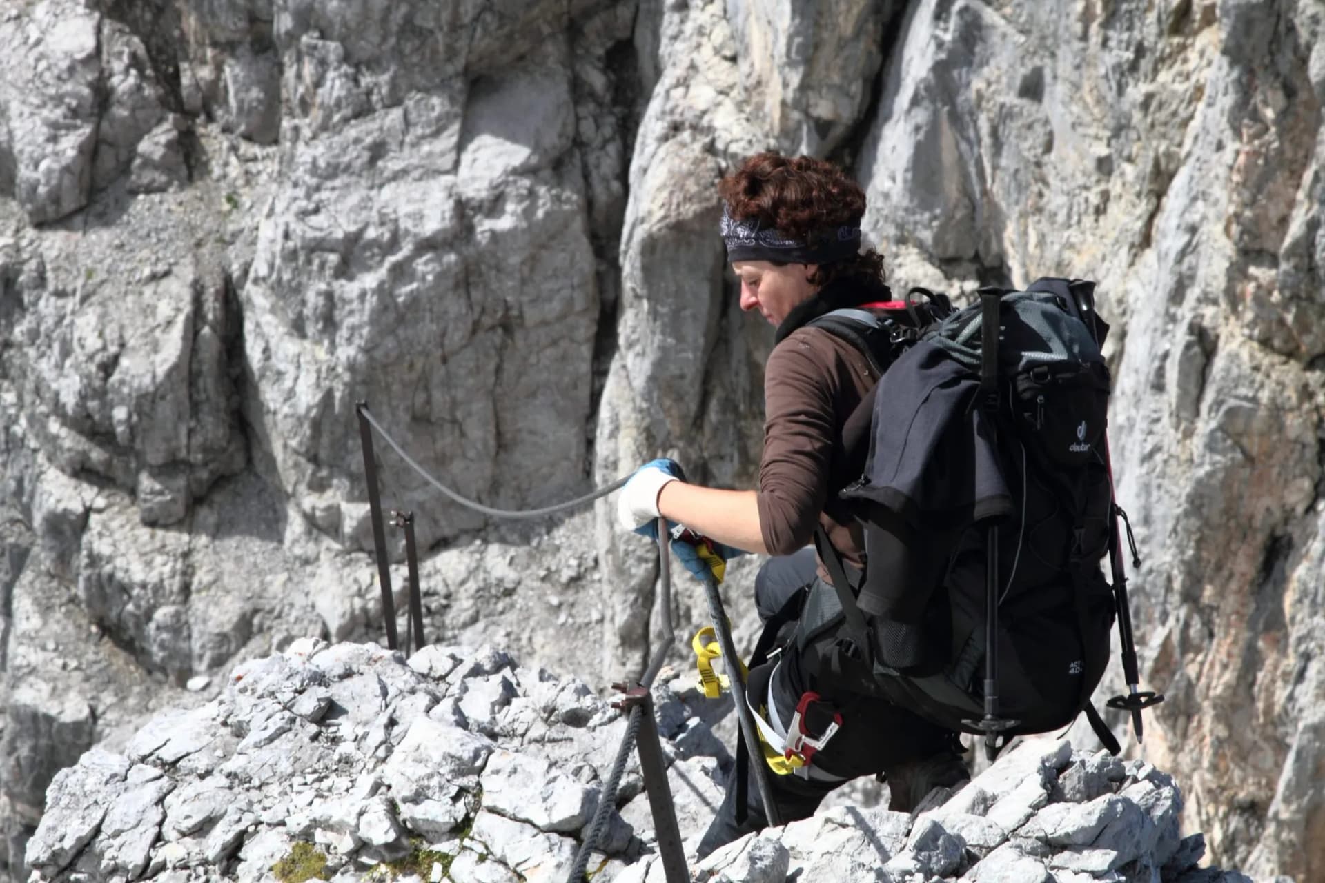 Hiker with backpack clipping into via ferrata cable on steep, rocky mountain face. Watzmann.