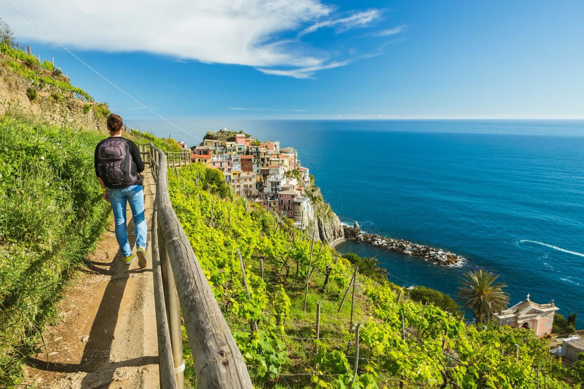 Hiker on trail above vineyards overlooking colorful coastal village and blue sea in Cinque Terre.