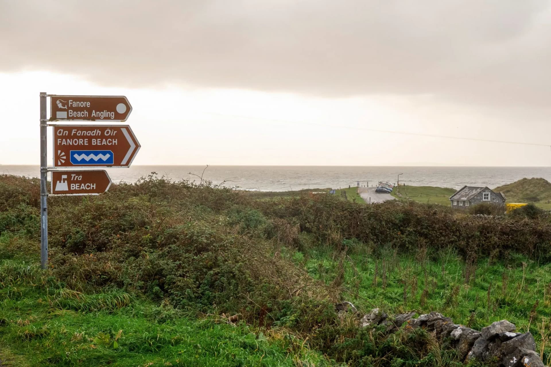 Sign Fanore beach and viewpoint on a metal fence. Popular travel destination on Wild Atlantic Way tourist route with amazing view on the ocean. Car park in the background.