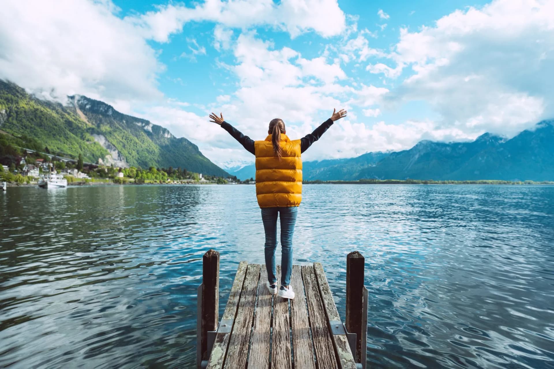 Young woman traveler with open arms standing on wooden bridge and enjoying great view on Geneva lake in Switzerland