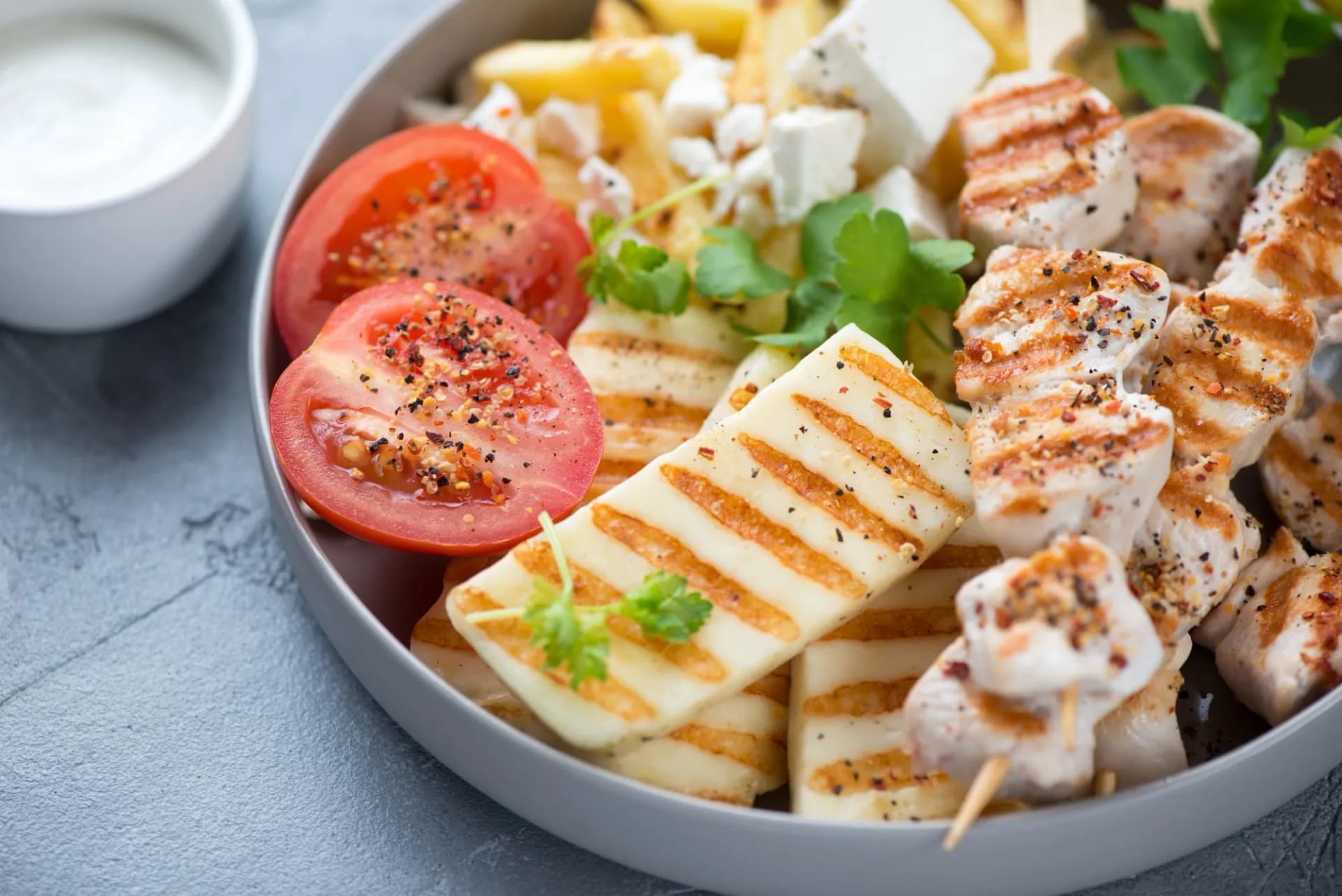 Close-up of grilled haloumi cheese, souvlaki skewers and potato fries, selective focus, studio shot