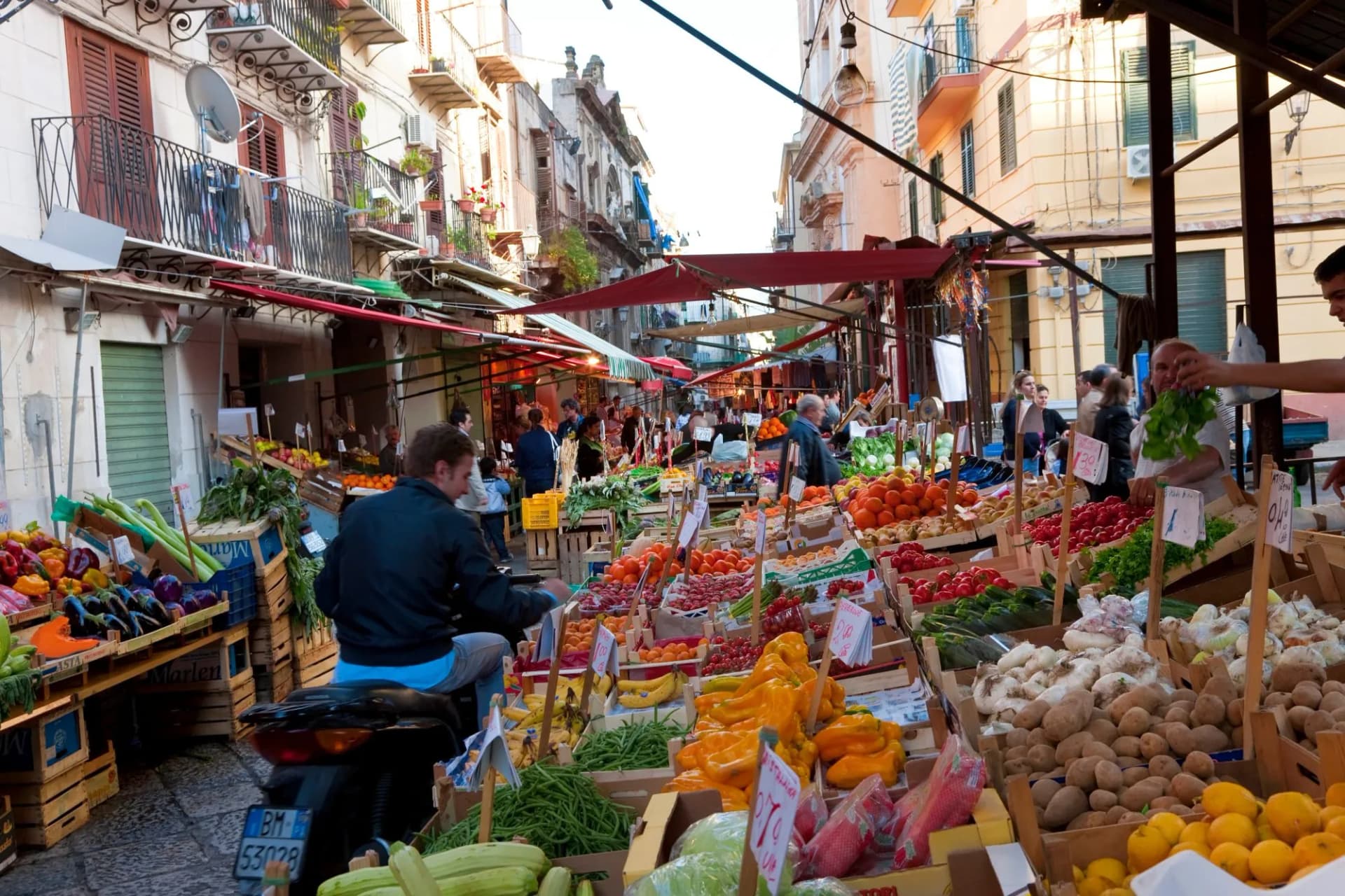 Produce market stalls lining a narrow street with apartment buildings in Palermo, Sicily.