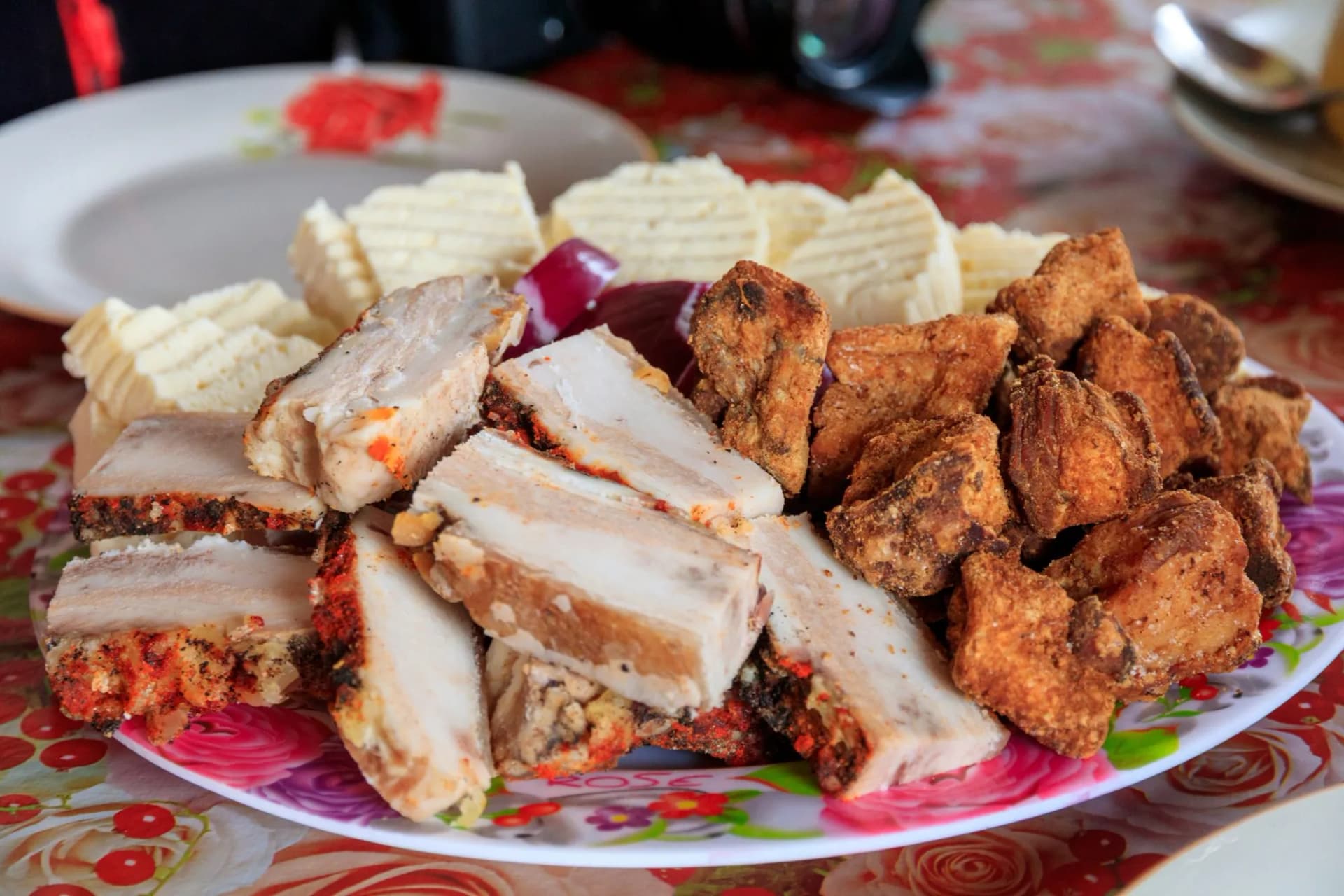 Platter of sliced cured pork belly, fried pork pieces, and butter served with red onion in Romania.