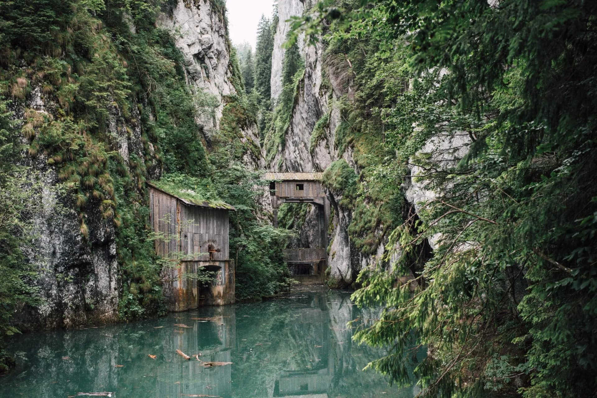 Old hydropower building, mirrored in the emerald water of Scropoasa. Artificial dam lake in the Romanian Carpathian Mountains. Trekking summer attraction for tourists.