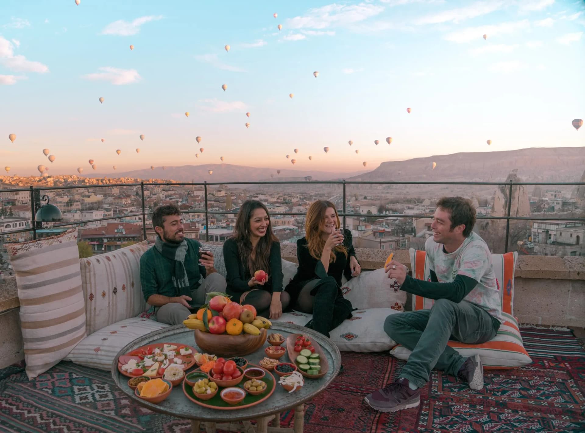 Four friends or two couples have fun whilst having breakfast outdoor with fruits, breads and drinks with a beautiful view to the balloons in Cappadocia, Turkey
