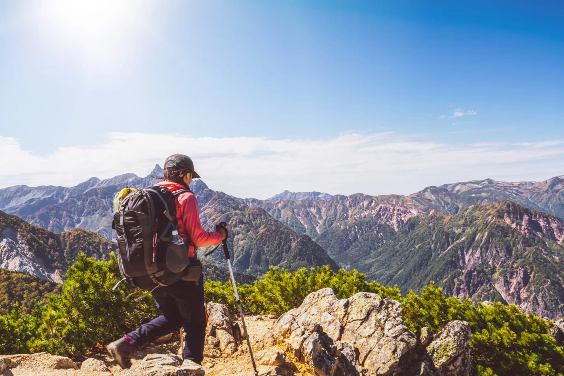 Hiker with backpack and trekking poles overlooks vast, rugged mountain ranges in the Northern Alps, Japan.