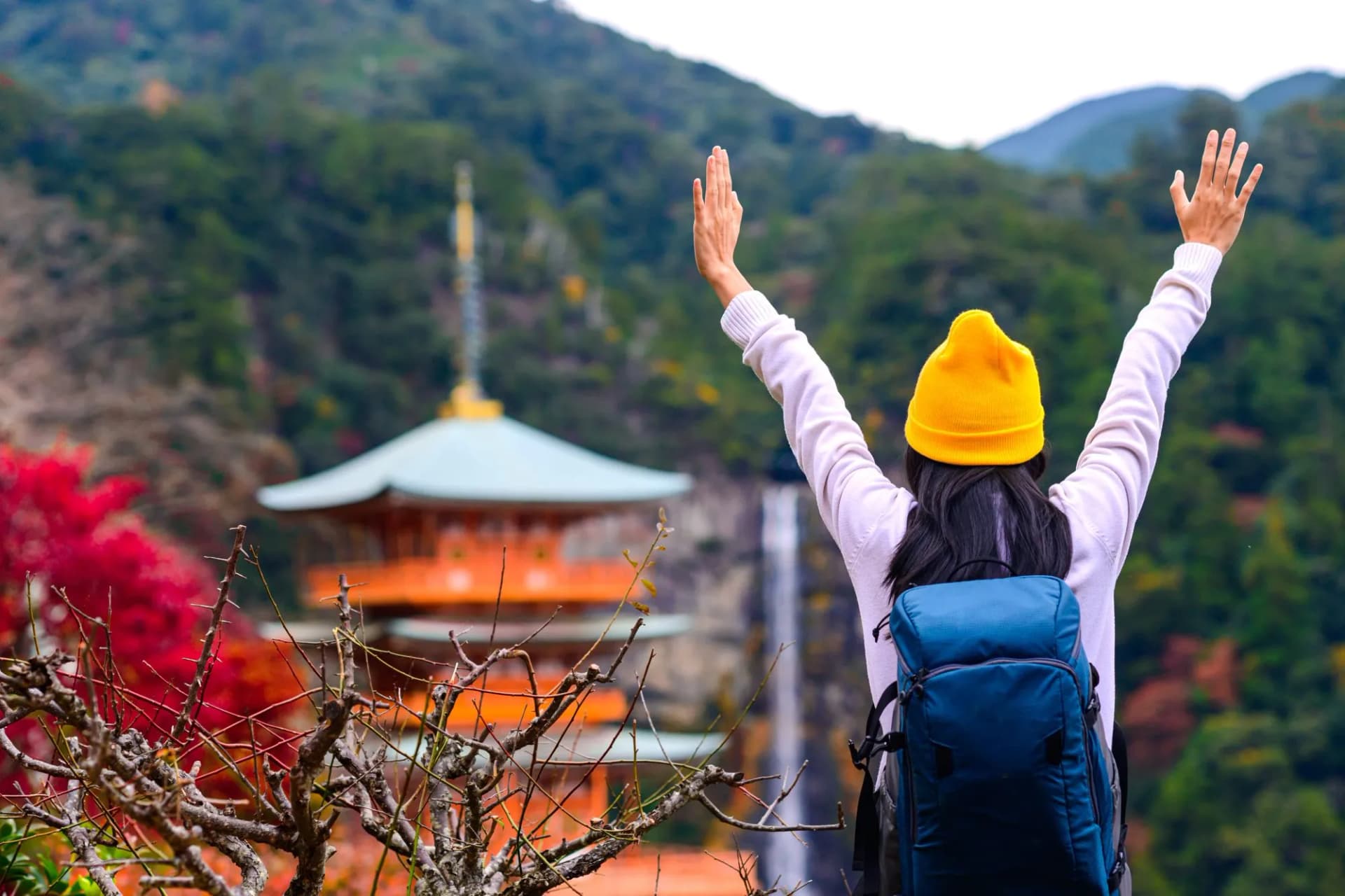 Hiker with arms raised in front of Nachi Taisha pagoda and waterfall.