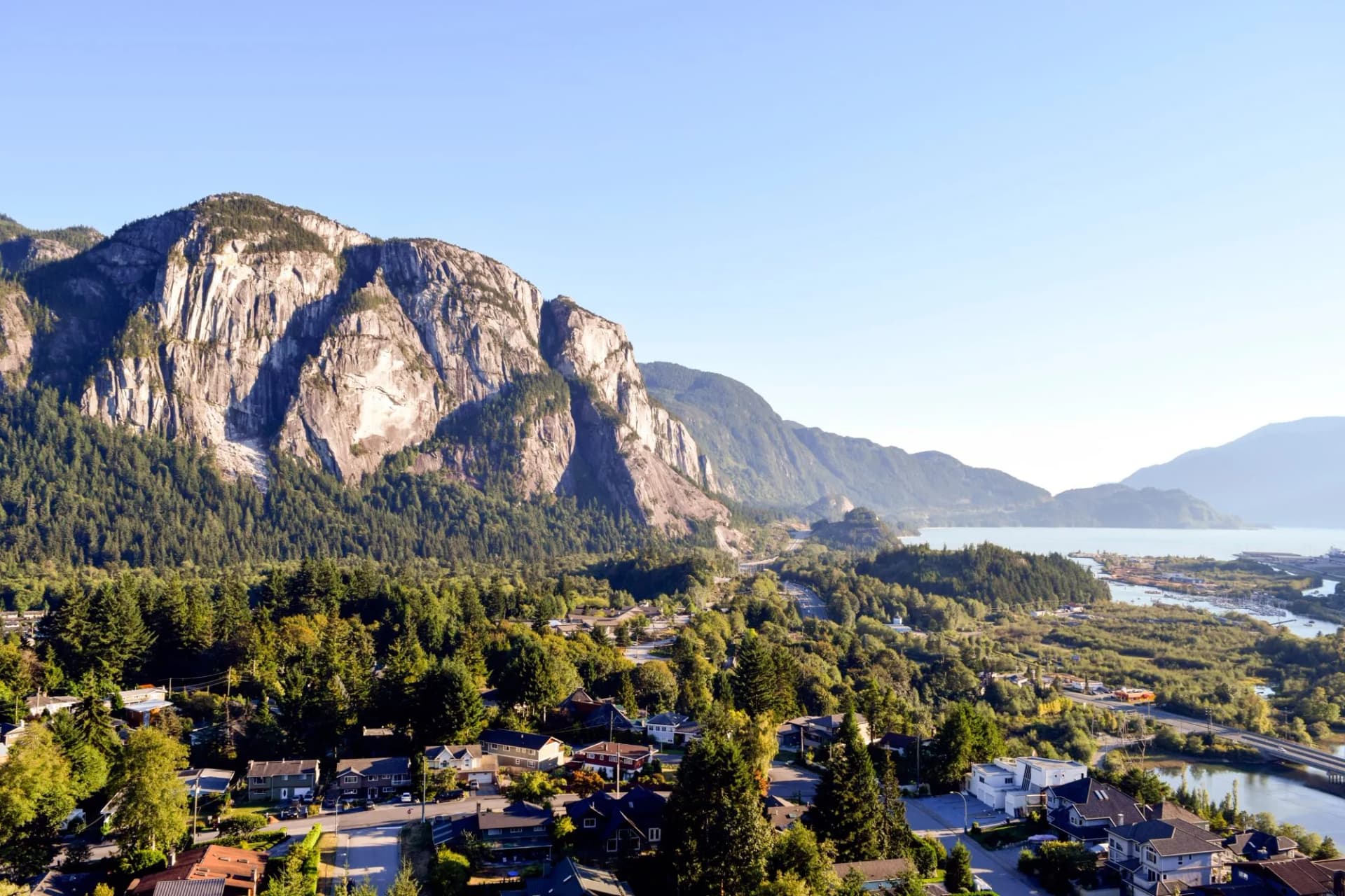 Residential area nestled below massive granite cliffs near a body of water in Squamish.
