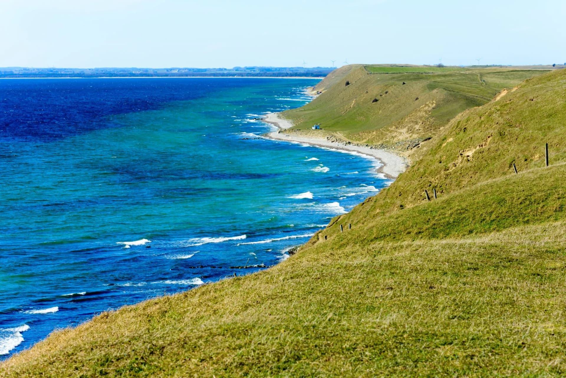 Grass covered coastal hills in spring. Weather is sunny and calm. Small house on the beach gives scale. Kaseberga coastline in Skane, Sweden.