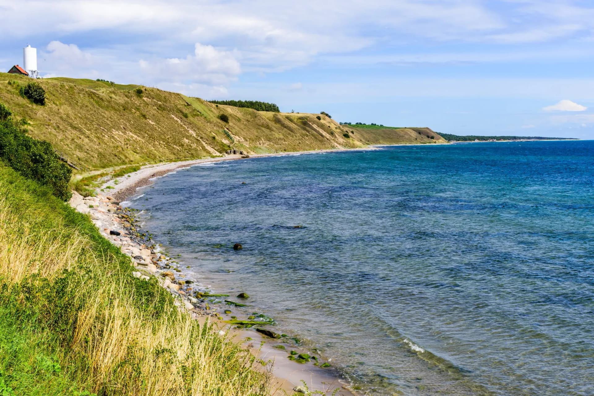 Sandy coastal slopes covered in dry grass in an ocean bay. White silo at a farm visible. Southern Skane in Sweden.