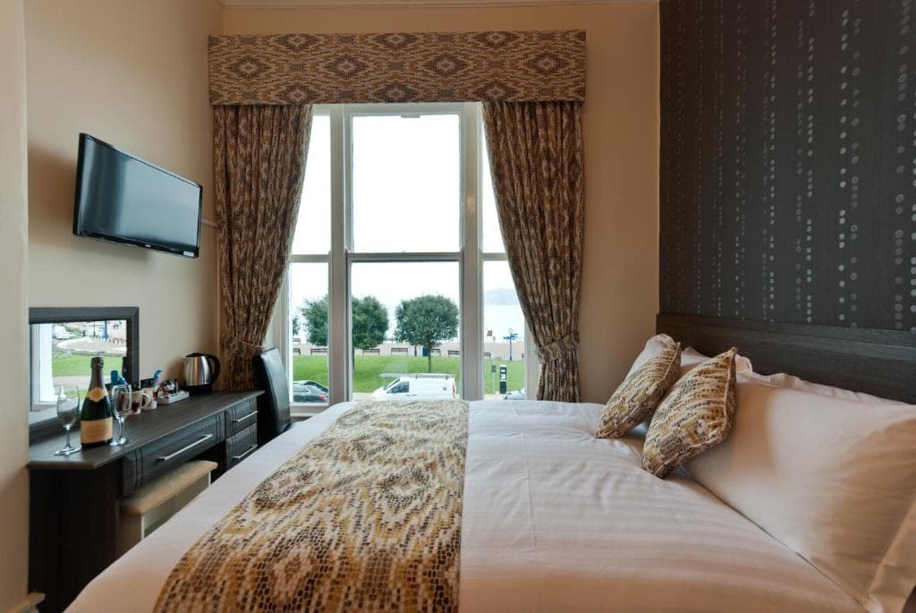 Hotel room with a large bed, patterned runner, and window view of the coast at Lauriston & Lawton Court Hotel, Llandudno.