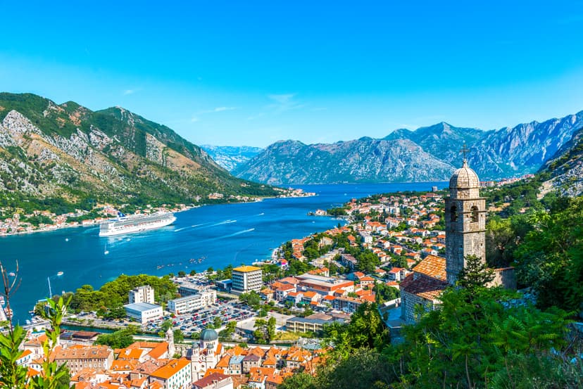 Cruise ship in the Bay of Kotor, Montenegro, with historic town buildings and surrounding mountains.