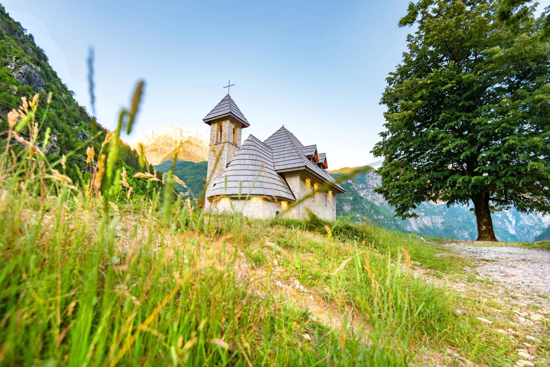 Stone church in Theth National Park set against green mountains and tall grass.