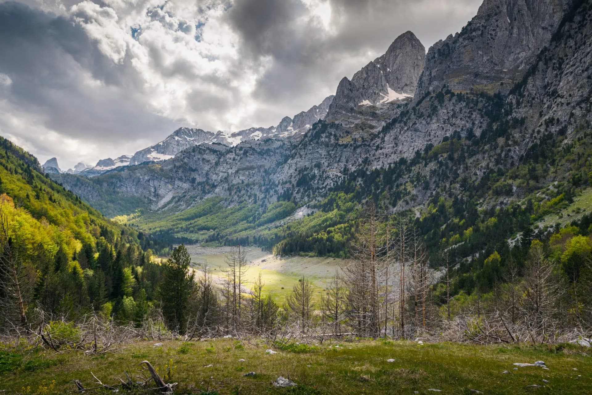 Mountain valley in Ropojana Valley with rocky peaks, green slopes, and dramatic cloudy sky
