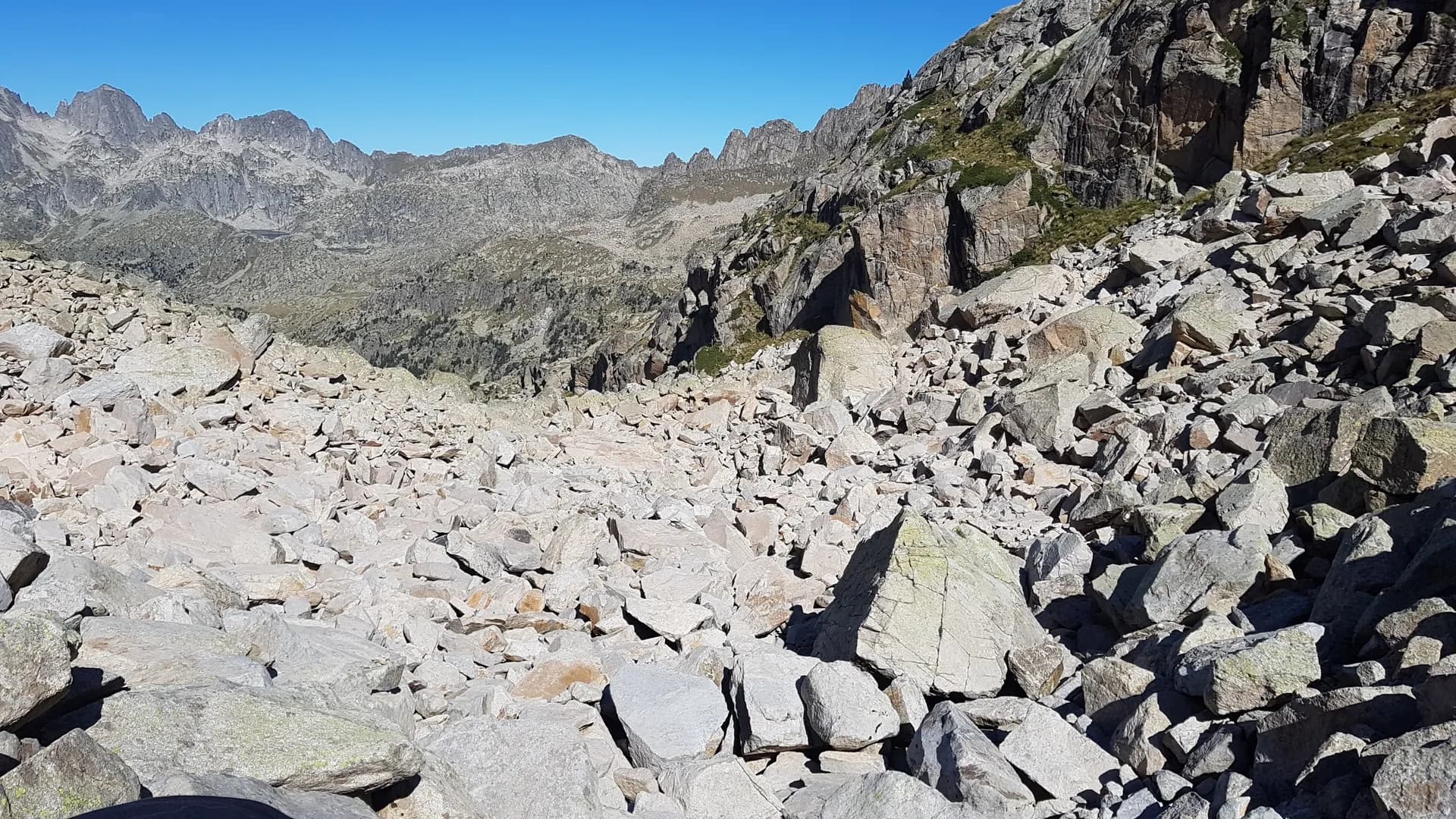 Rocky mountain landscape with a steep scree slope and rugged peaks under a clear blue sky.