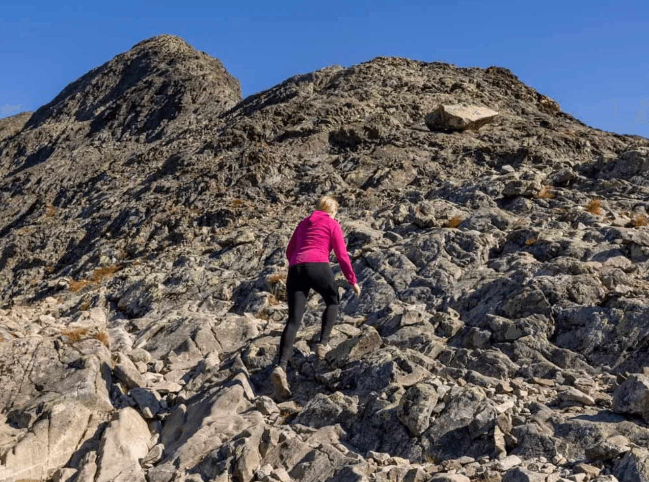 Hiker in a pink jacket climbing a rocky mountain trail in Jotunheimen.