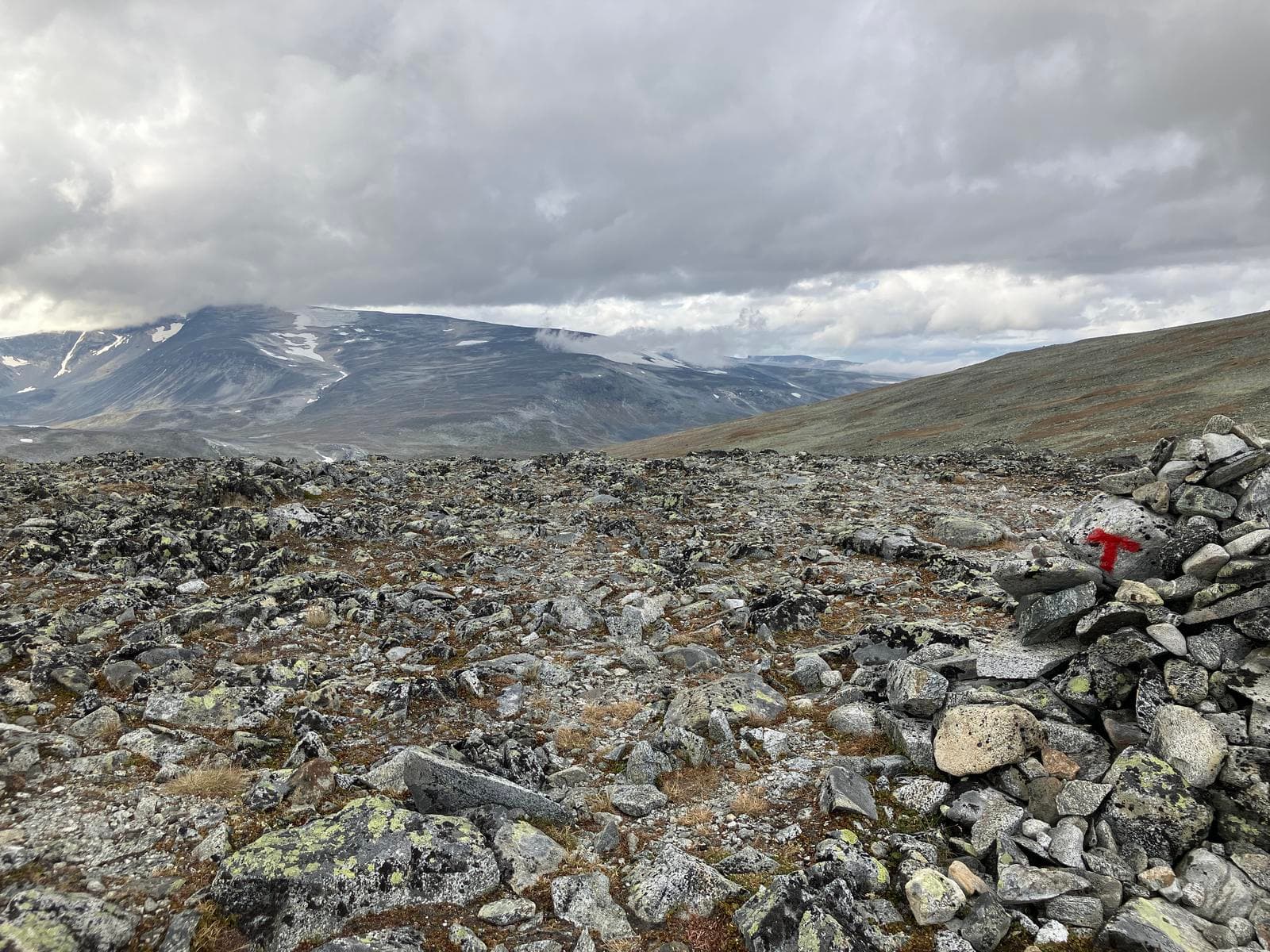 Rocky mountain landscape in Jotunheimen with a red trail marker on a stone cairn under a cloudy sky.