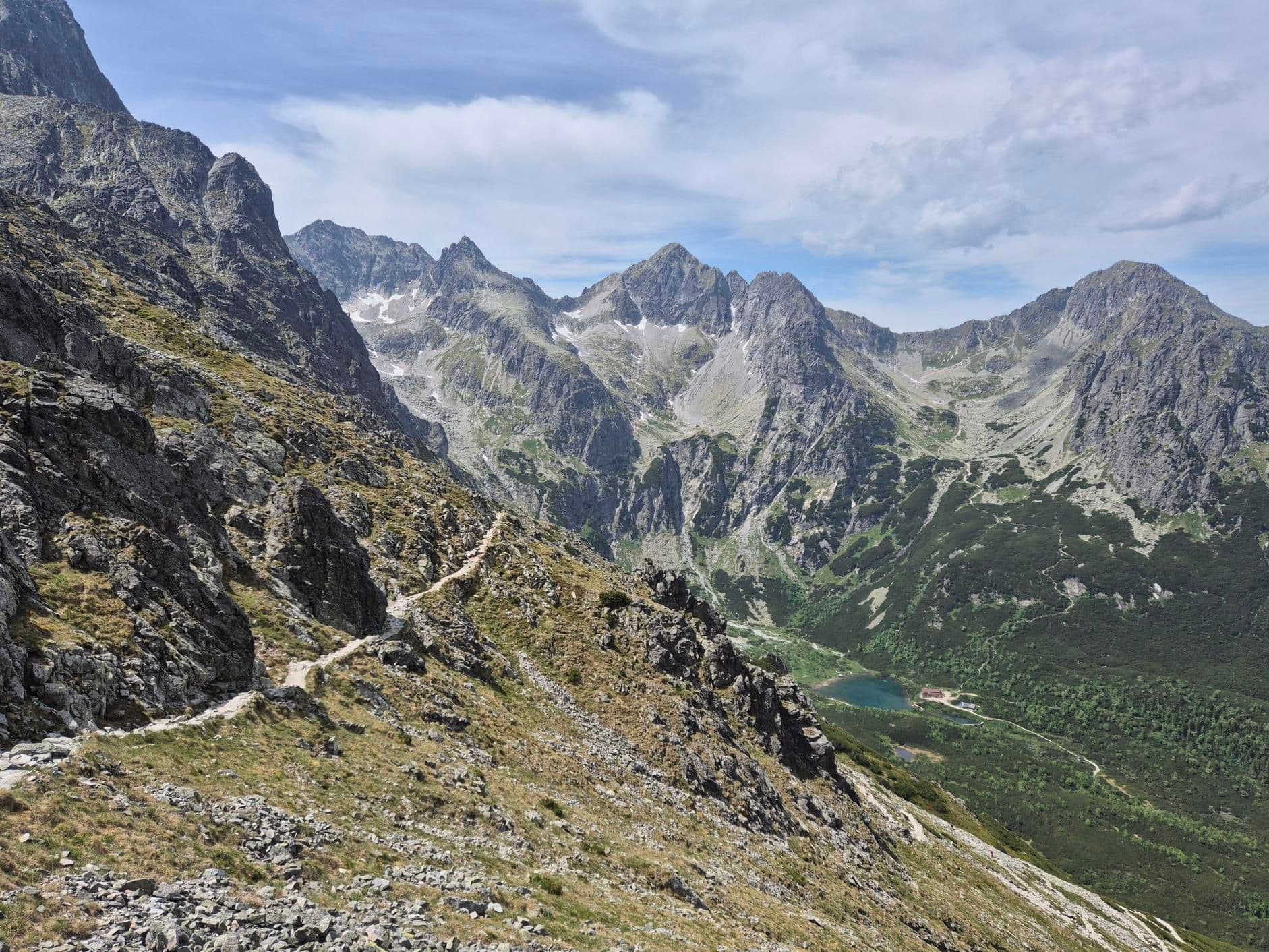 Hiking trail on rocky mountain slopes with alpine peaks and a valley lake in the High Tatras.