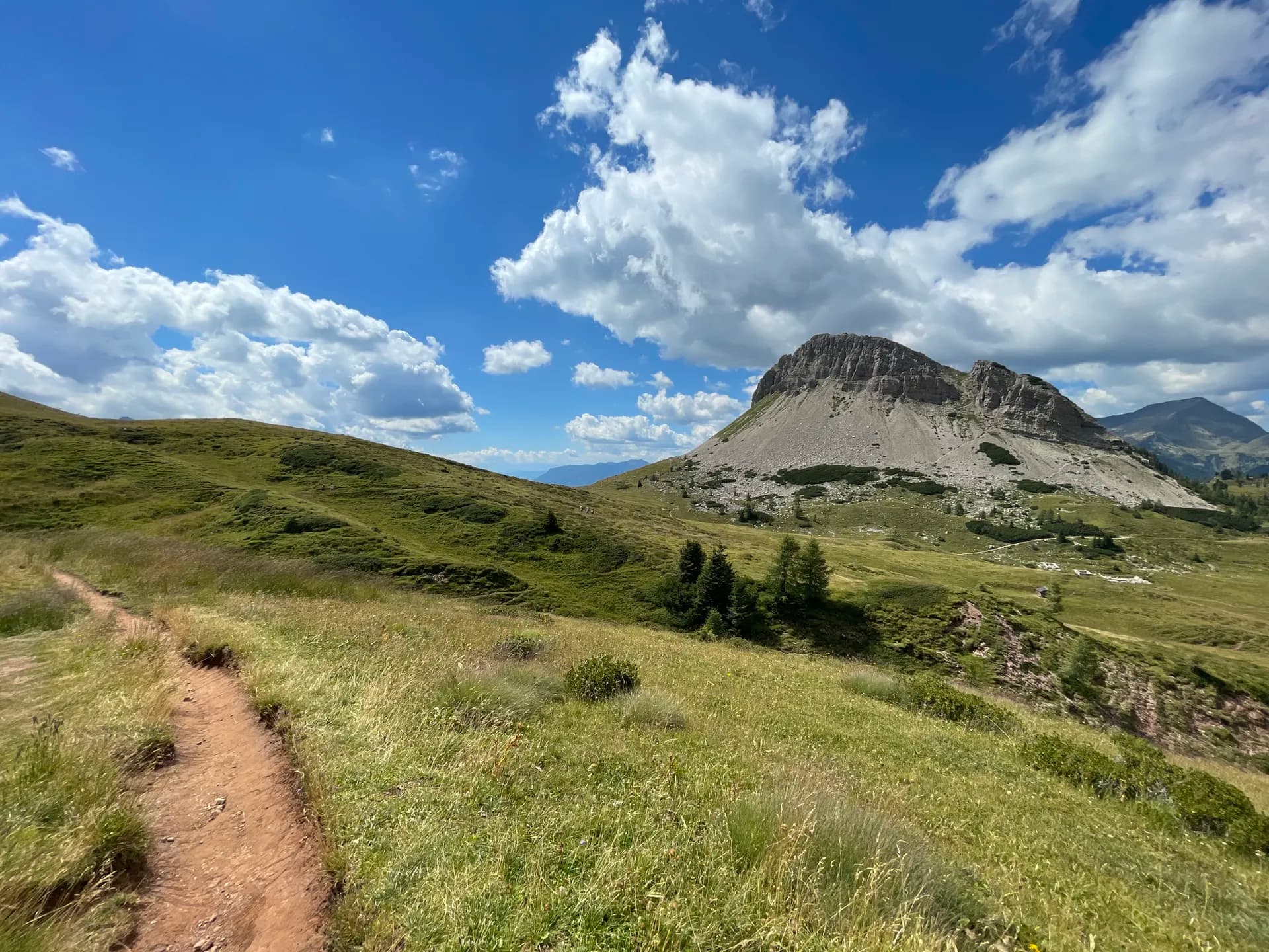 Hiking trail in the Pale di San Martino mountains with green alpine meadows and blue sky.