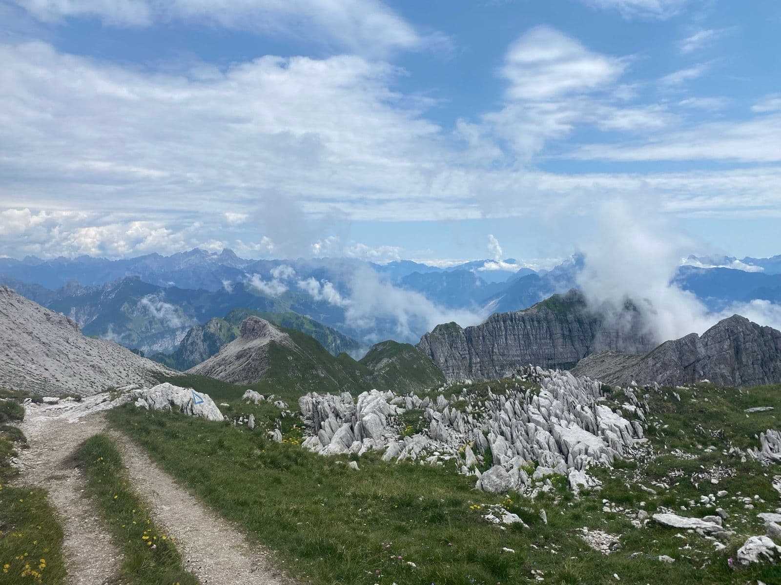 Hiking trail through rocky alpine mountain landscape with clouds and distant peaks.