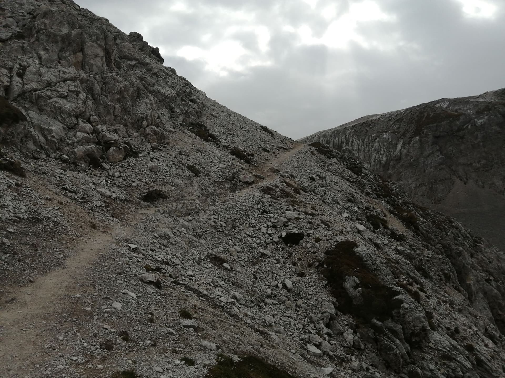 Narrow hiking trail winding up a rocky mountain slope under a cloudy sky.