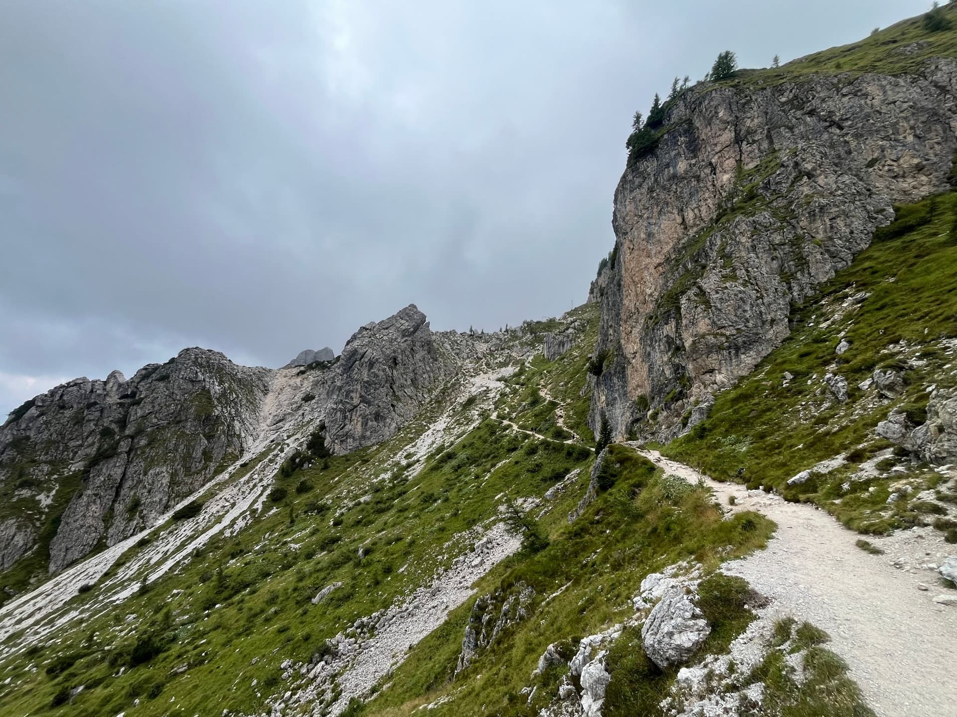 Hiking trail winding through steep rocky mountain slopes under a cloudy sky.