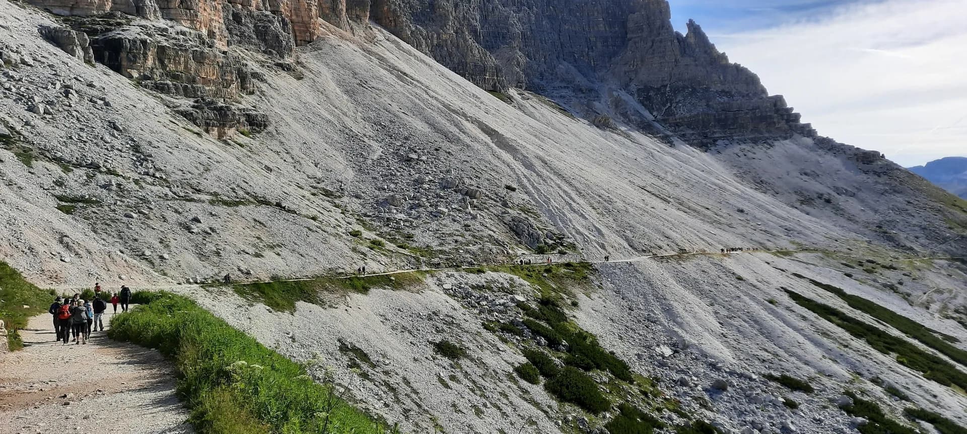 Hikers on a narrow mountain trail beneath the rocky peaks of the Dolomites.