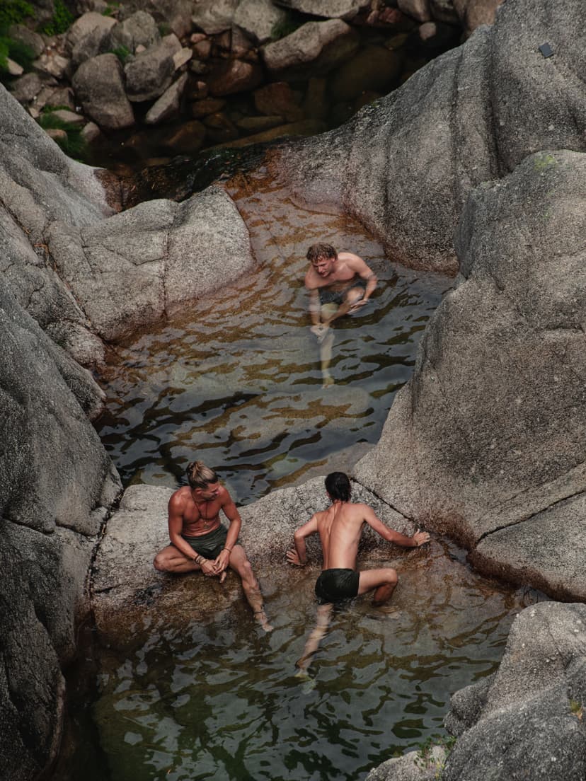 Three men swimming and sitting among natural rock pools and boulders
