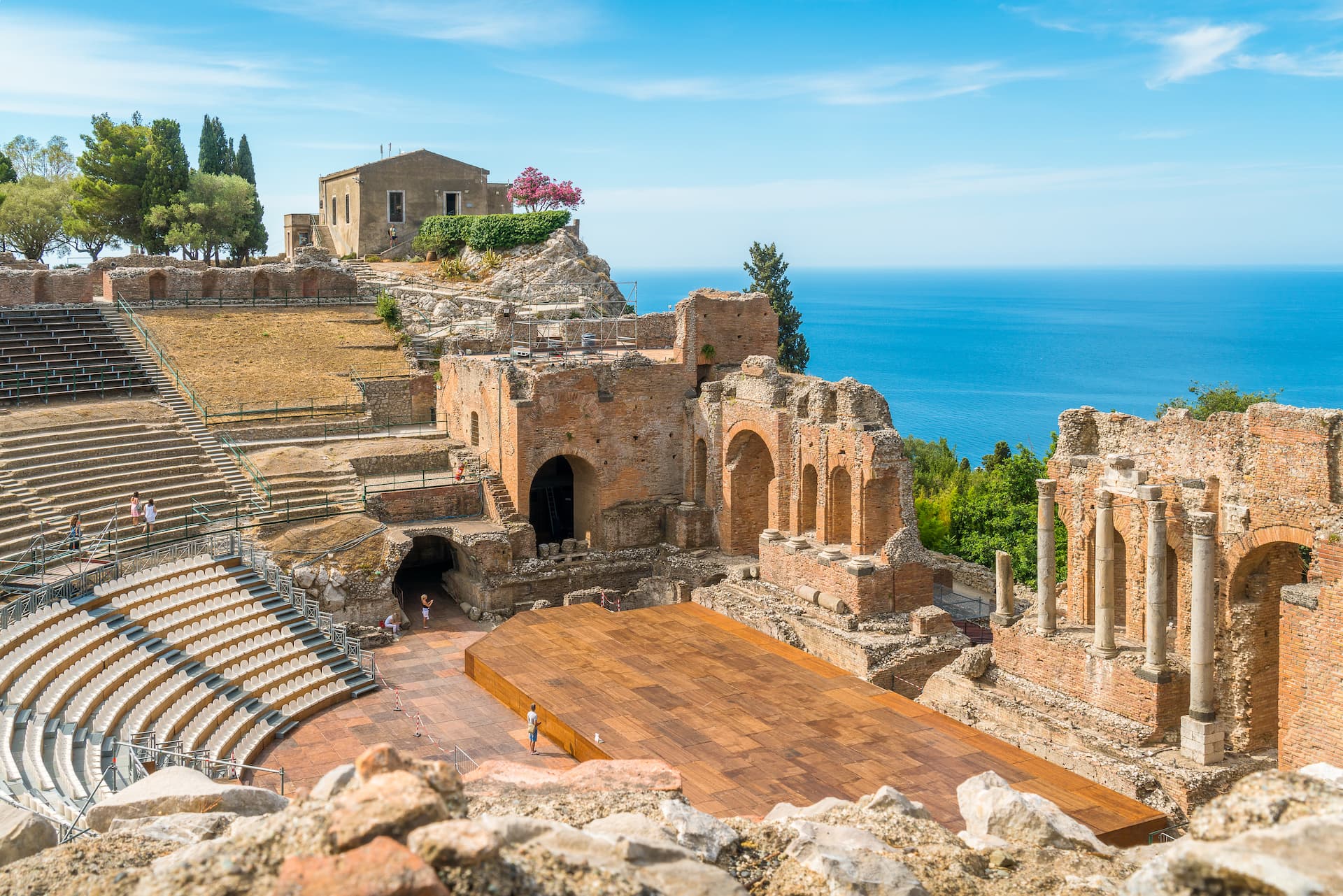 Ancient Roman theater ruins overlooking the bright blue sea under a clear sky in Greece.
