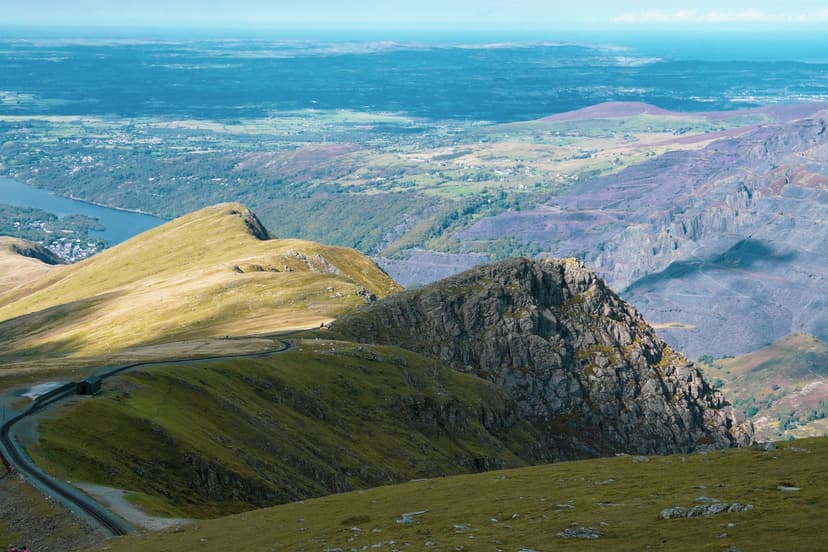 Snowdonia aerial mountain view with railway track winding across grassy slopes and rocky peaks overlooking distant valleys...