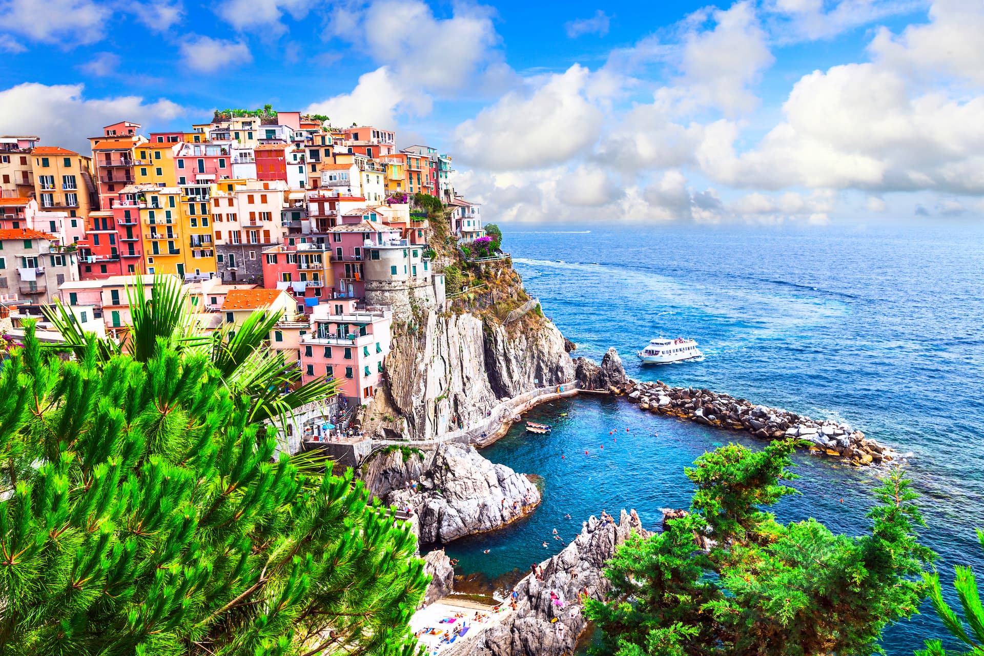 Colorful cliffside village overlooking bright blue Mediterranean Sea with boats and swimmers